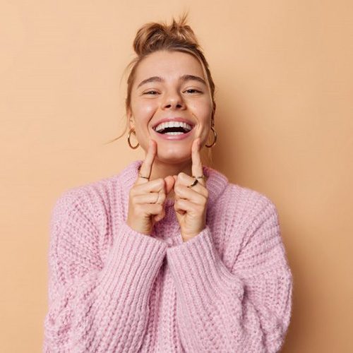 Woman smiling and pointing proudly at her beautiful teeth