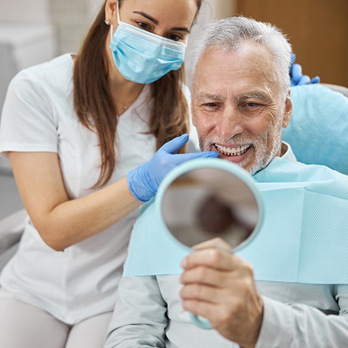 An older man admiring his new dental implant with a hand mirror