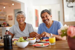 Man in blue t-shirt eating breakfast with woman in grey t-shirt at a brown table