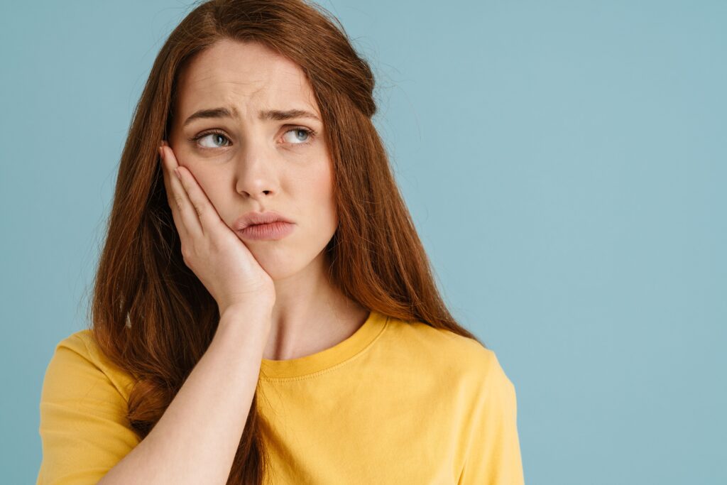 Woman with red hair in yellow shirt holding hand to jaw in pain