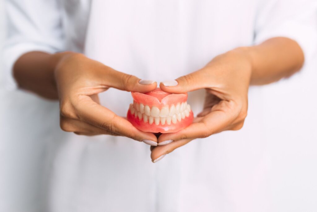 Two hands with manicured nails holding a full set of dentures